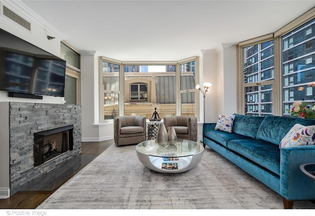 living room featuring a stone fireplace, wood-type flooring, and ornamental molding