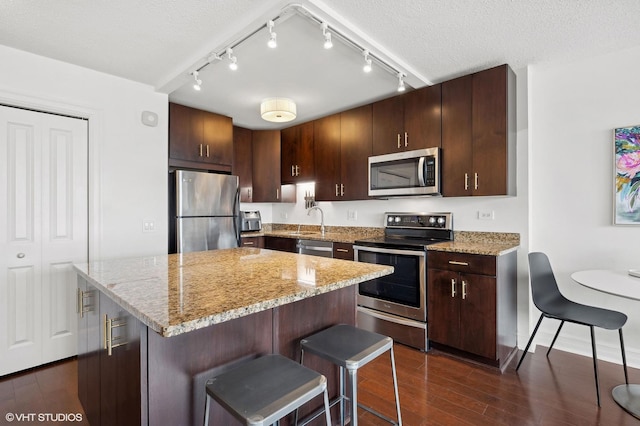 kitchen featuring dark hardwood / wood-style flooring, a center island, light stone counters, stainless steel appliances, and a textured ceiling