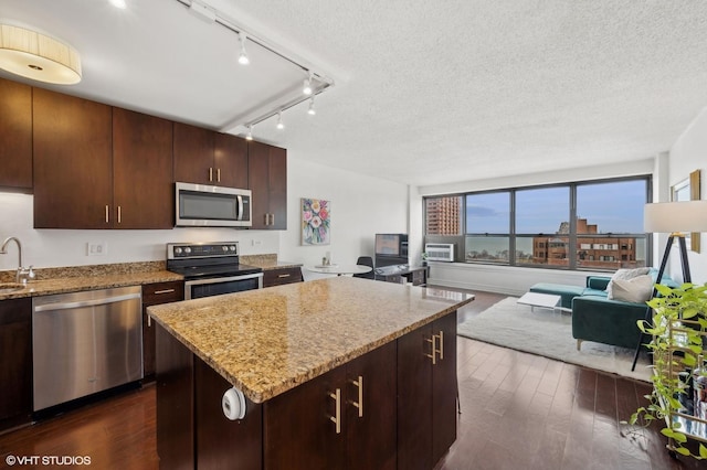 kitchen with a textured ceiling, dark hardwood / wood-style floors, a kitchen island, stainless steel appliances, and light stone countertops