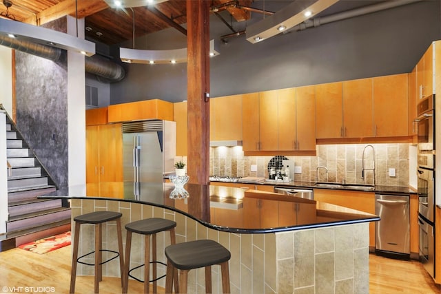 kitchen with appliances with stainless steel finishes, high vaulted ceiling, sink, backsplash, and light wood-type flooring