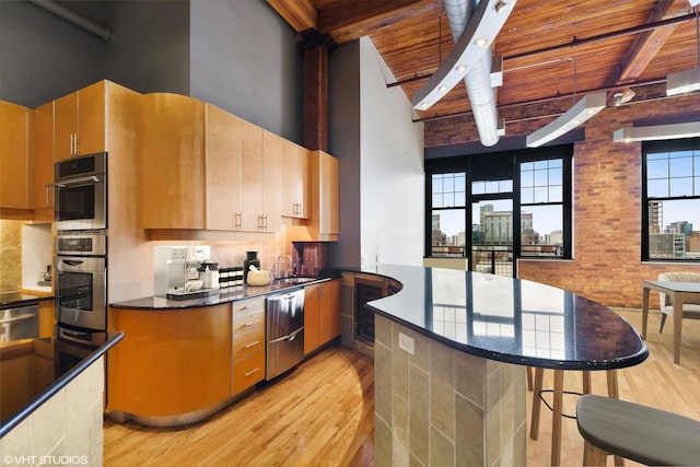 kitchen with stainless steel appliances, a kitchen bar, beam ceiling, and light hardwood / wood-style flooring