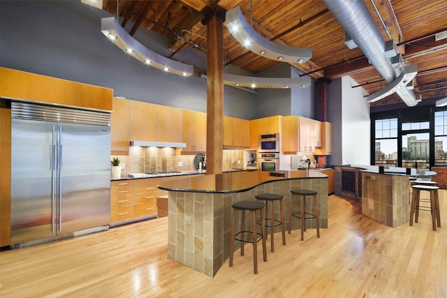 kitchen with wood ceiling, built in refrigerator, a kitchen island, a towering ceiling, and decorative backsplash