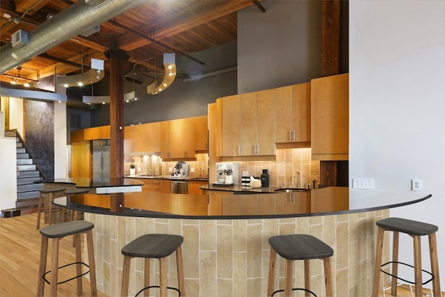 kitchen with tasteful backsplash, beamed ceiling, a kitchen bar, a high ceiling, and stainless steel appliances