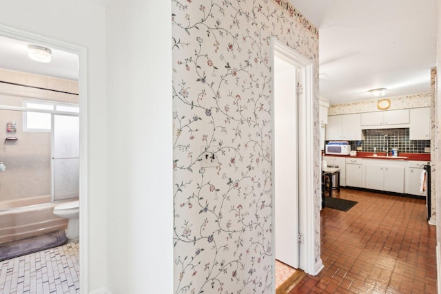 corridor with brick floor, wallpapered walls, and a sink