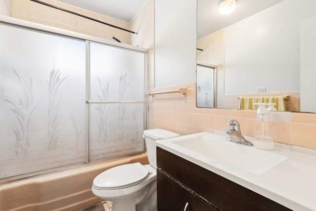 bathroom with enclosed tub / shower combo, toilet, vanity, and tile walls