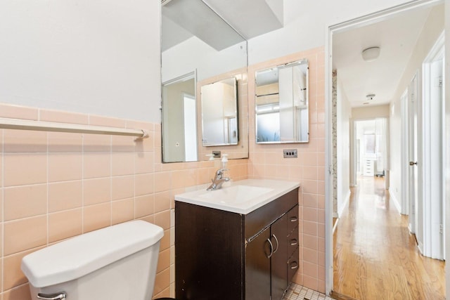 bathroom with toilet, wood finished floors, vanity, and tile walls