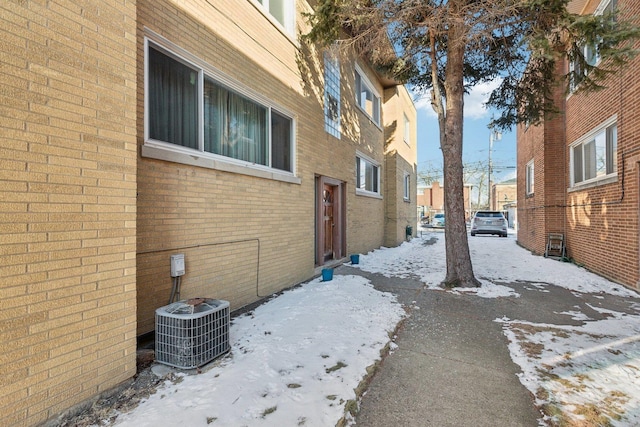 snow covered property featuring central AC unit and brick siding