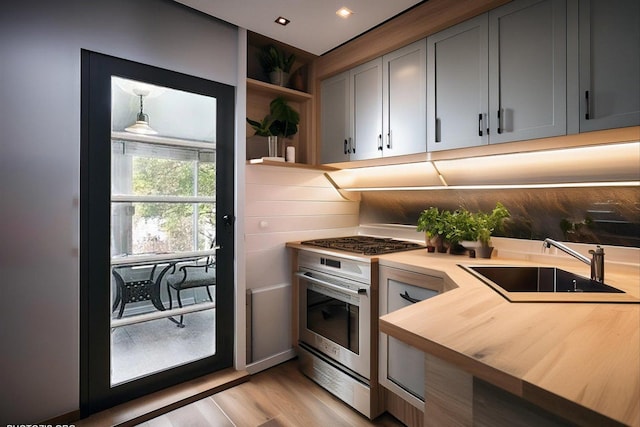 kitchen featuring stainless steel gas range oven, light wood finished floors, a sink, gray cabinetry, and open shelves