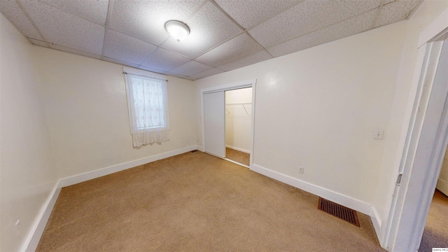 unfurnished bedroom featuring light carpet, a drop ceiling, and a closet