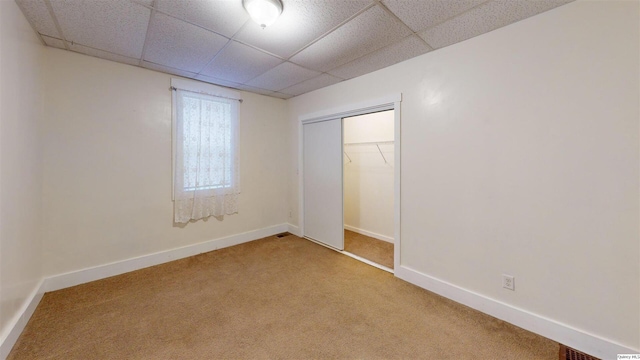 unfurnished bedroom with a drop ceiling, light colored carpet, and a closet