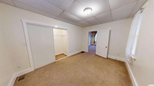 unfurnished bedroom featuring a paneled ceiling, light colored carpet, and a closet