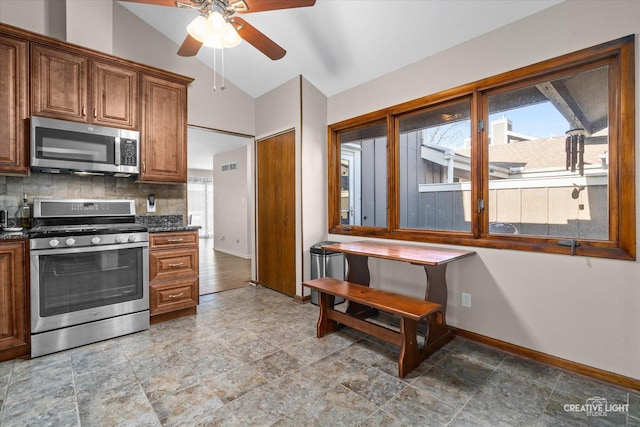 kitchen featuring ceiling fan, dark stone countertops, backsplash, stainless steel appliances, and vaulted ceiling