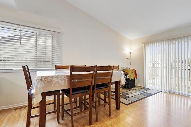 dining space featuring light wood finished floors, baseboards, and vaulted ceiling