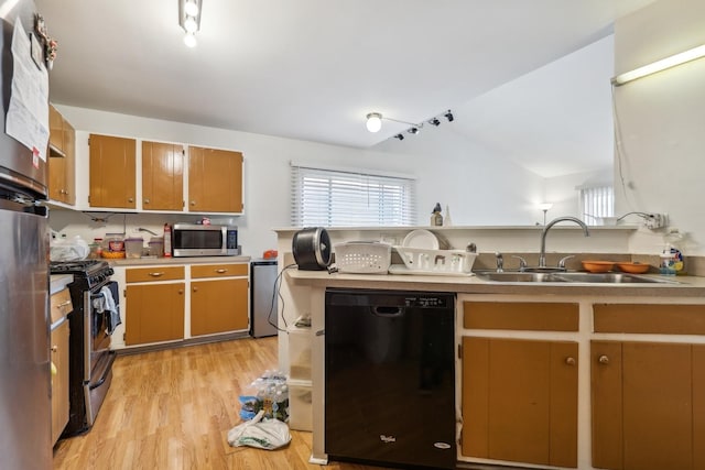 kitchen featuring stainless steel appliances, a sink, light wood-style floors, vaulted ceiling, and light countertops