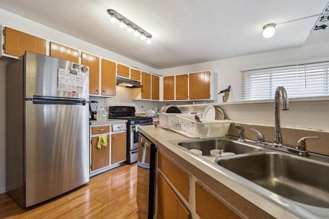 kitchen featuring brown cabinets, stainless steel appliances, light wood-style flooring, a sink, and under cabinet range hood