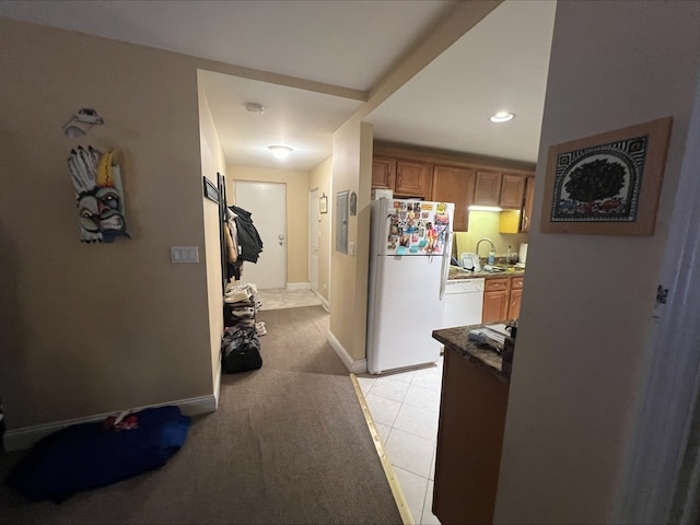 hall featuring light tile patterned floors, baseboards, and a sink