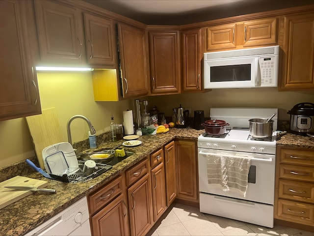 kitchen featuring dark stone countertops, sink, white appliances, and light tile patterned floors