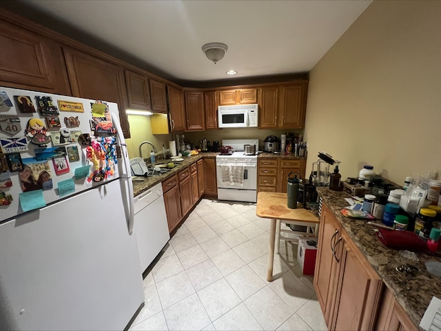 kitchen with brown cabinetry, white appliances, dark stone countertops, and light tile patterned floors