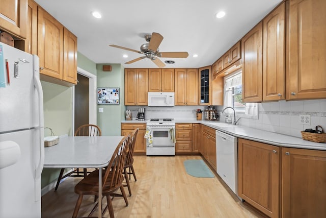 kitchen featuring a sink, light wood-type flooring, white appliances, and tasteful backsplash