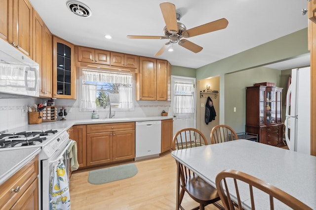 kitchen featuring visible vents, a sink, tasteful backsplash, white appliances, and light wood finished floors