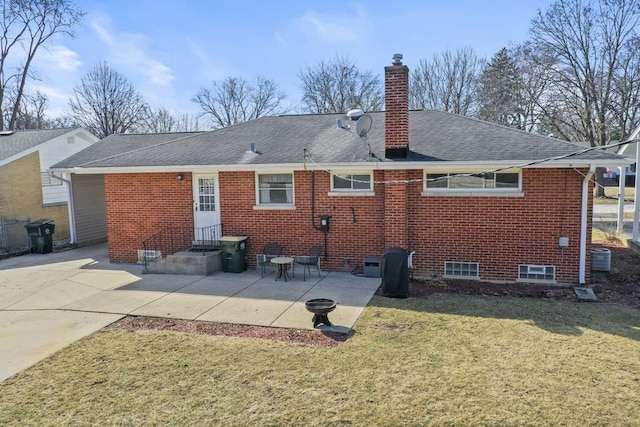 rear view of house with brick siding, roof with shingles, a chimney, a yard, and a patio