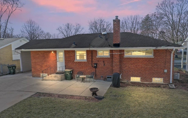 rear view of house with a patio, a yard, brick siding, central AC unit, and a chimney