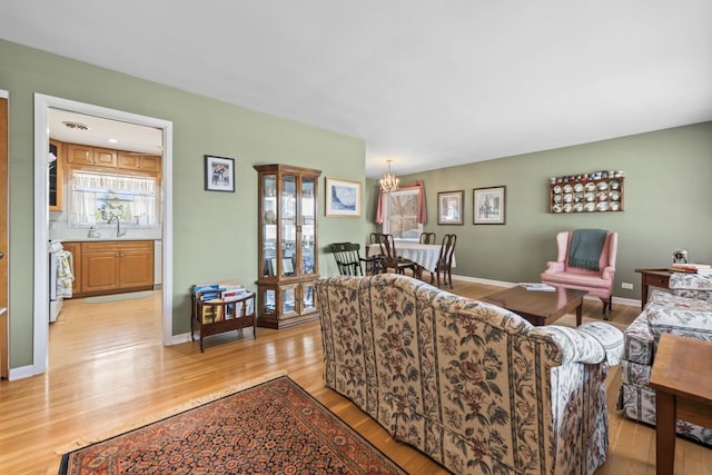 living room featuring light wood finished floors, a notable chandelier, and baseboards