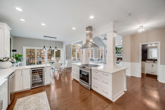 kitchen featuring appliances with stainless steel finishes, white cabinetry, hanging light fixtures, island exhaust hood, and beverage cooler