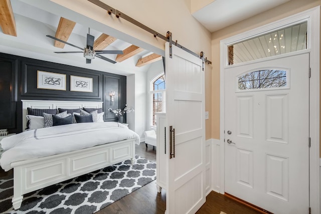 bedroom featuring ceiling fan, a barn door, dark wood-type flooring, and beam ceiling