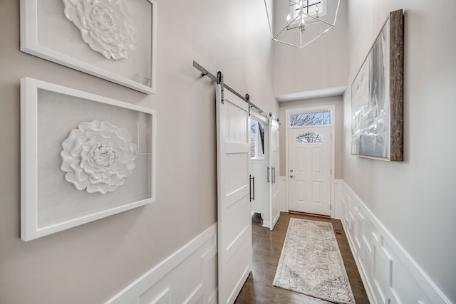 entryway with dark hardwood / wood-style floors, a notable chandelier, a barn door, and a high ceiling