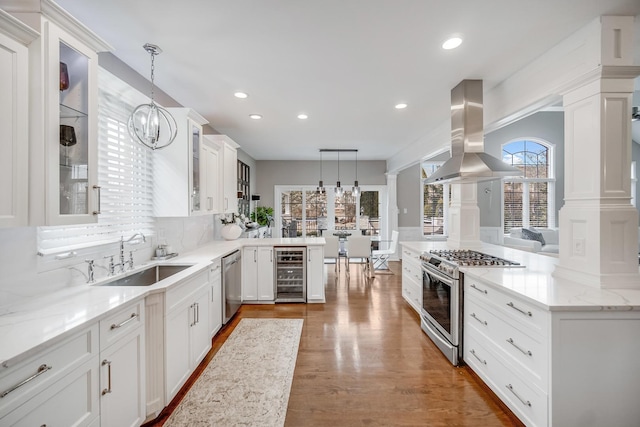 kitchen featuring island range hood, hanging light fixtures, kitchen peninsula, stainless steel appliances, and beverage cooler