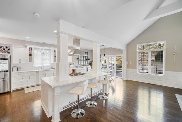 kitchen with a breakfast bar area, decorative light fixtures, island exhaust hood, decorative columns, and white cabinets