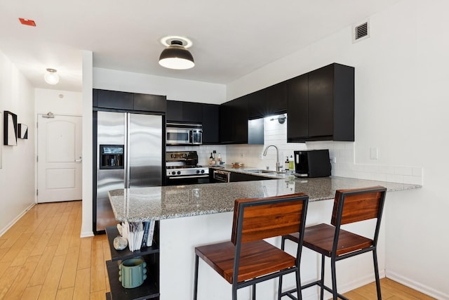 kitchen with sink, backsplash, a kitchen breakfast bar, stainless steel appliances, and kitchen peninsula