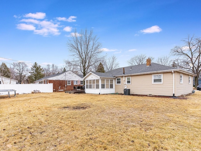 back of house featuring a sunroom, a chimney, a trampoline, fence, and a yard