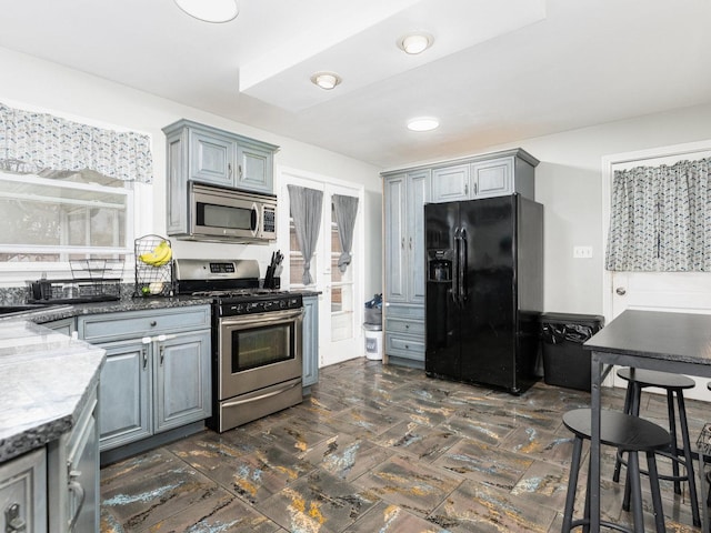 kitchen with stone counters, appliances with stainless steel finishes, gray cabinets, and a sink