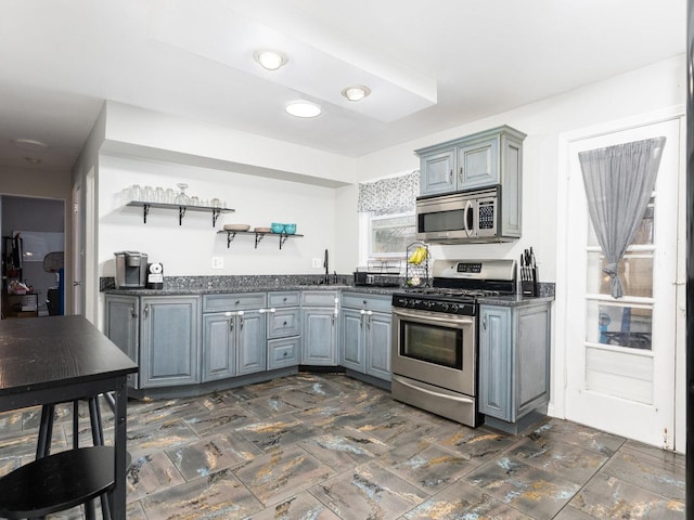 kitchen featuring open shelves, stainless steel appliances, a sink, and gray cabinetry