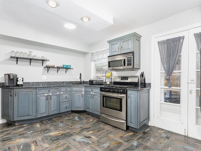 kitchen with dark stone countertops, gray cabinets, stainless steel appliances, open shelves, and a sink