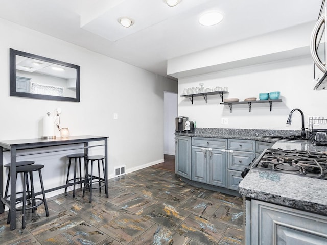 kitchen with black gas range, visible vents, baseboards, open shelves, and a sink