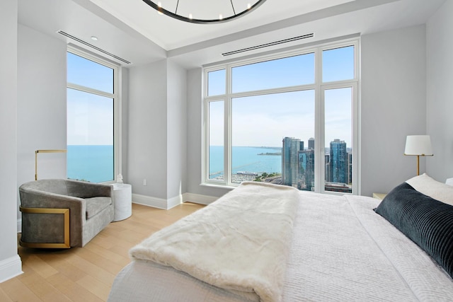 bedroom with multiple windows, a water view, an inviting chandelier, and light hardwood / wood-style floors