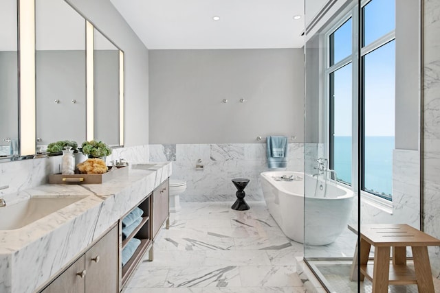 bathroom with tile walls, a bathing tub, a water view, vanity, and toilet