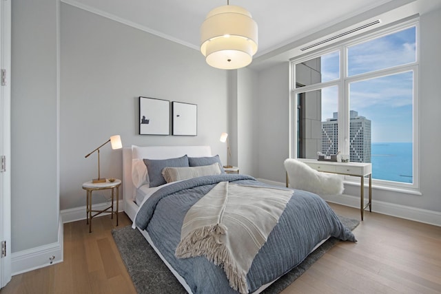 bedroom with crown molding, wood-type flooring, and a water view