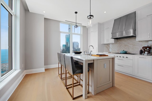 kitchen with white cabinetry, wall chimney range hood, decorative light fixtures, and a center island with sink