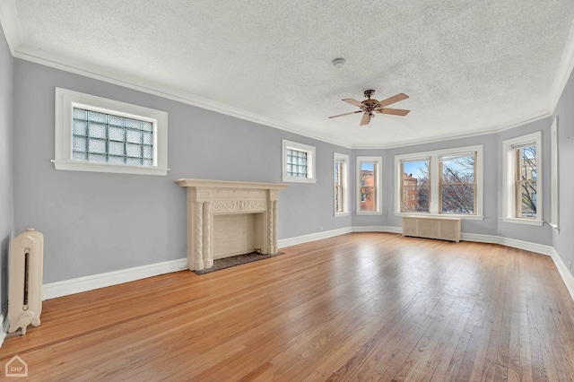 unfurnished living room with radiator, a fireplace, ornamental molding, ceiling fan, and light hardwood / wood-style flooring