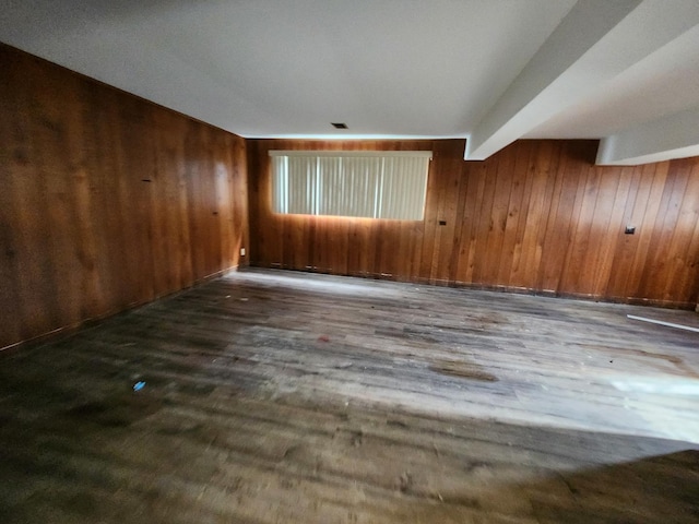 empty room featuring dark wood-type flooring, wooden walls, and beamed ceiling