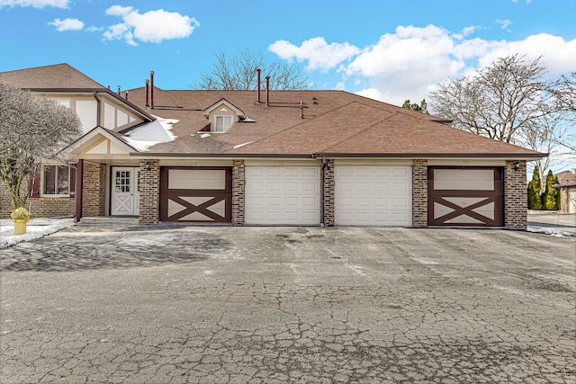 view of front of house featuring a garage, brick siding, and roof with shingles