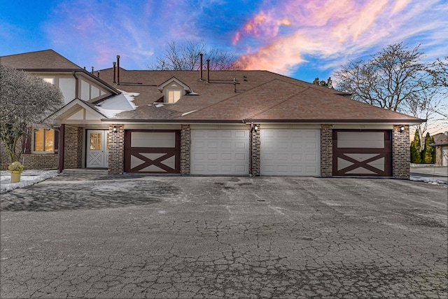 view of front facade with a garage, brick siding, roof with shingles, and aphalt driveway