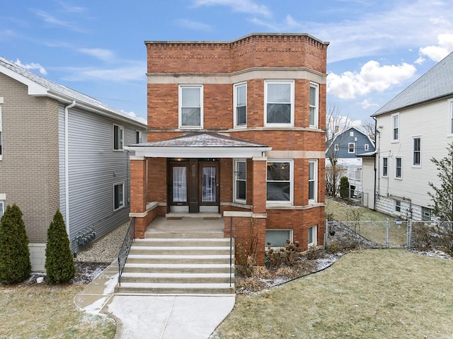 view of front facade featuring a front yard, french doors, brick siding, and fence