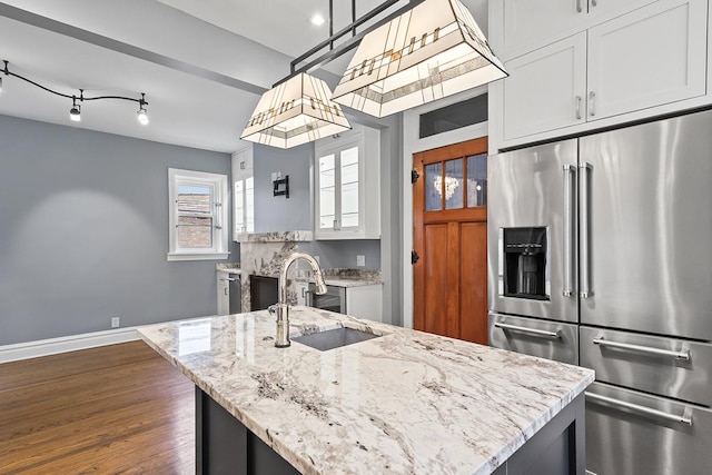 kitchen featuring a sink, baseboards, high end fridge, light stone countertops, and a center island with sink