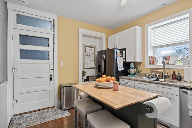 kitchen featuring sink, white cabinets, a kitchen bar, stainless steel dishwasher, and black refrigerator with ice dispenser