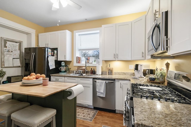 kitchen with white cabinetry, appliances with stainless steel finishes, light stone countertops, and a breakfast bar area